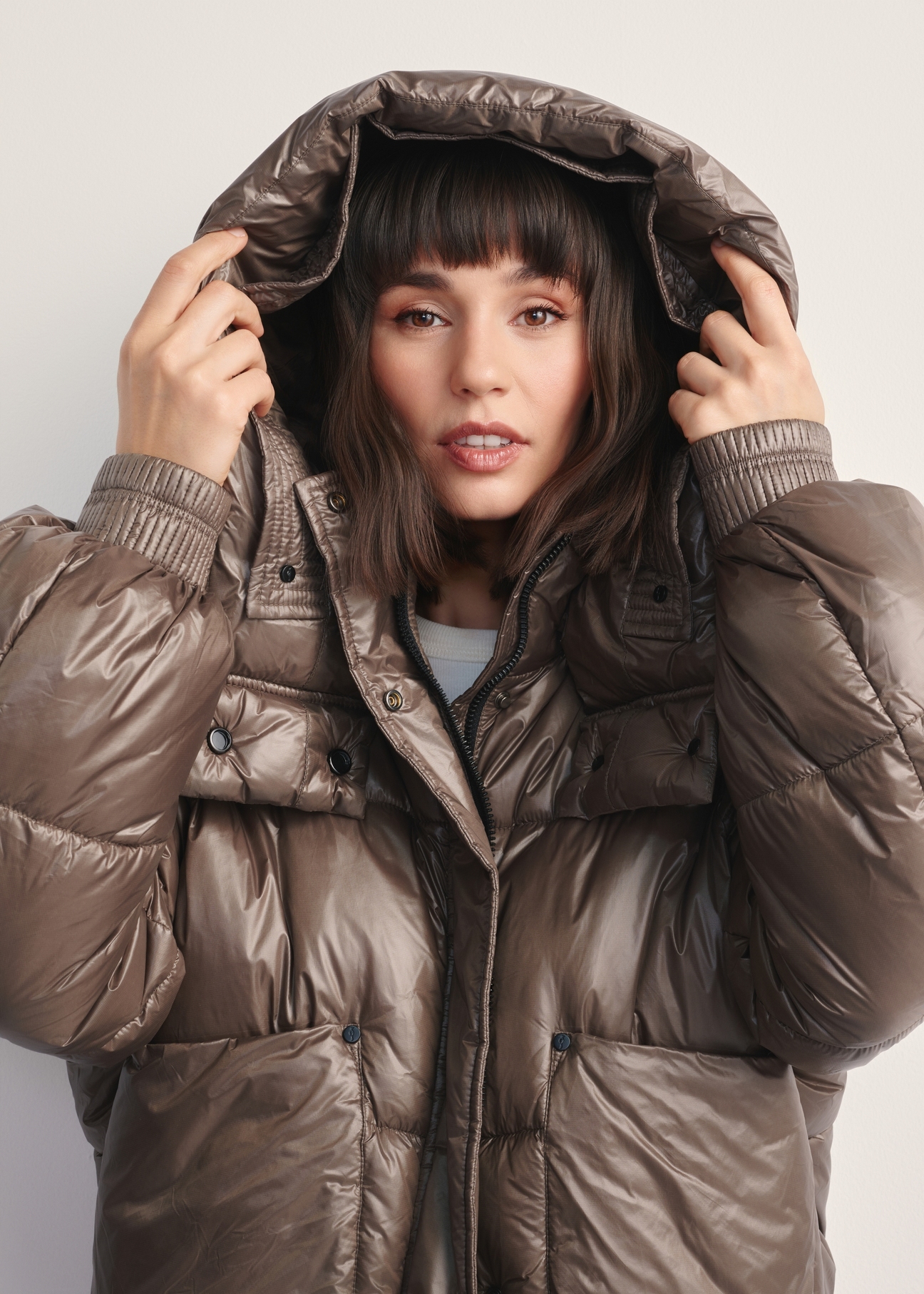 Dámska krátka hnedá bunda KURDT-0608-82(Z25), pohľad na produkt s kapucňou na modeli na svetlom pozadí.