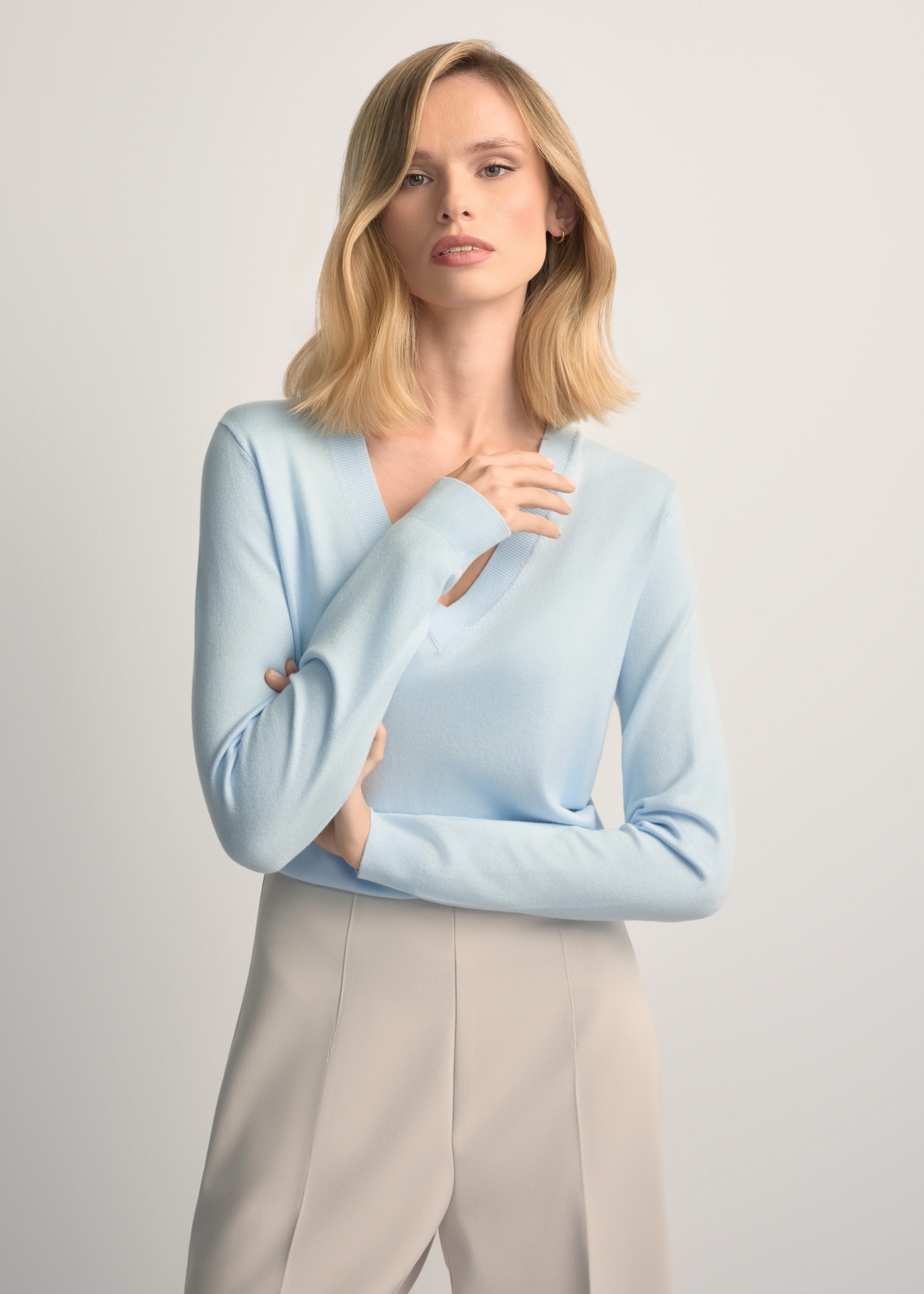 Svetlomodrý sveter s výstrihom do V SWEDT-0201-7A(W26) - pohľad spredu na výrobok, na modelke, na svetlom pozadí. Viditeľná polovica siluety.