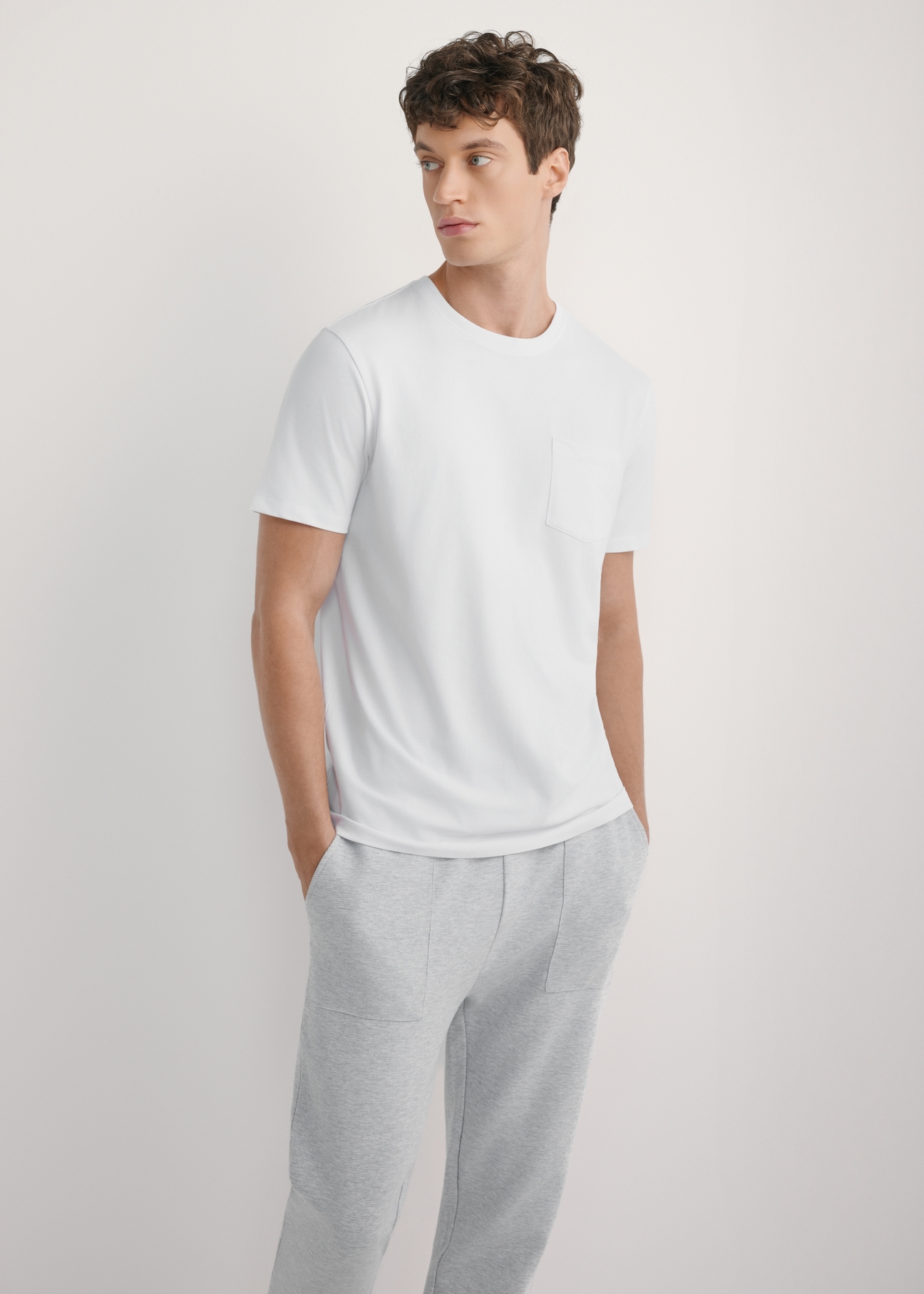 Pánske biele tričko TSHMT-0137-0A(W26) - pohľad spredu na produkt, na modelke, na svetlom pozadí. Viditeľná silueta po kolená.