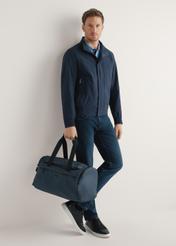 Námornícka modrá cestovná taška TORMN-0412-7D(W26) - pohľad na produkt, ktorú drží modelka, na svetlom pozadí. Viditeľné celé telo.