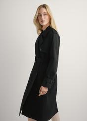 Dlhá čierna dámska bunda v podobe kabáta KURDT-0512-99(W25), pohľad na produkt z boku na modelke, viditeľná polovica siluety.