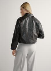 Dámska hnedá kožená krátka bunda KURDS-0593-1I(W26) - pohľad na výrobok zozadu, na modelke, na svetlom pozadí. Viditeľná silueta po kolená.