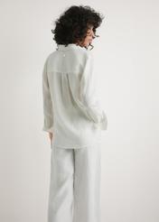 Dámska biela ľanová košeľa KOSDT-0163A-0B(W26) - pohľad na výrobok zozadu, na modelke, na svetlom pozadí. Viditeľná polovica siluety.