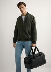 Čierna cestovná taška TORMN-0412-99(W26), pohľad na produkt v ruke modelky. Viditeľné celé telo.