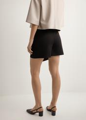 Dámske čierne culottes SZODT-0008-99(W26), pohľad na modelku zozadu. Viditeľná polovica siluety.