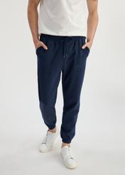 Pánske tepláky v tmavomodrej farbe SPOMT-0109-69(W25) - pohľad spredu na modelku na bielom pozadí. Viditeľná je polovica siluety.