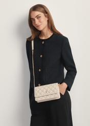 Malá prešívaná dámska kabelka v krémovej farbe TOREC-1150-0B(W26) - pohľad spredu na produkt, na modelke, na svetlom pozadí. Viditeľná silueta po pás.