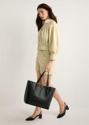 Čierna monogramová nákupná kabelka TOREC-1181-99(W26) - pohľad spredu na produkt, na modelke, na svetlom pozadí. Viditeľná je celá silueta.