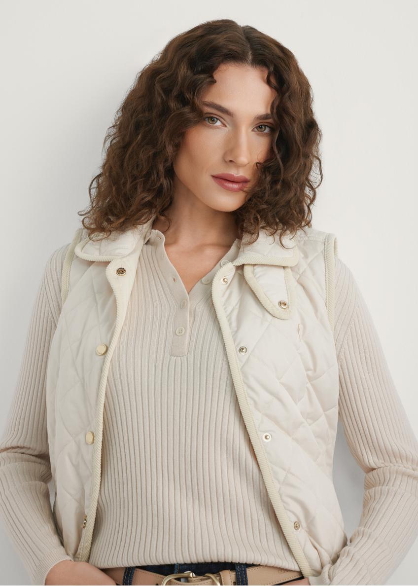 Svetlobéžová dámska prešívaná vesta KAMDT-0036-0B(W26) - pohľad spredu na výrobok, na modelke, na svetlom pozadí. Viditeľná polovica siluety.