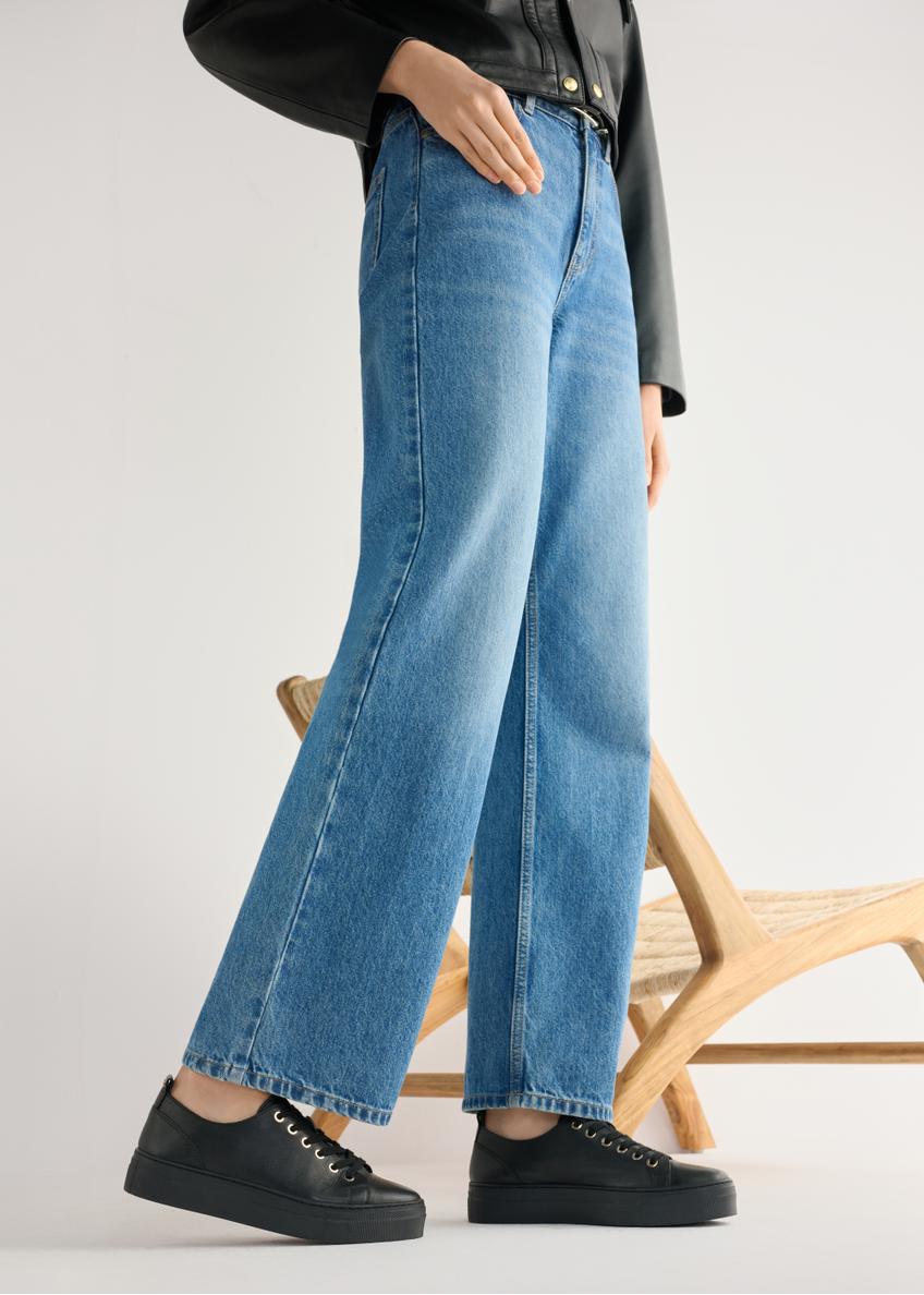 Dámske čierne kožené tenisky BUTYD-1062-99(W26) - bočný pohľad na produkt, na modelke, na svetlom pozadí. Viditeľná silueta po kolená.