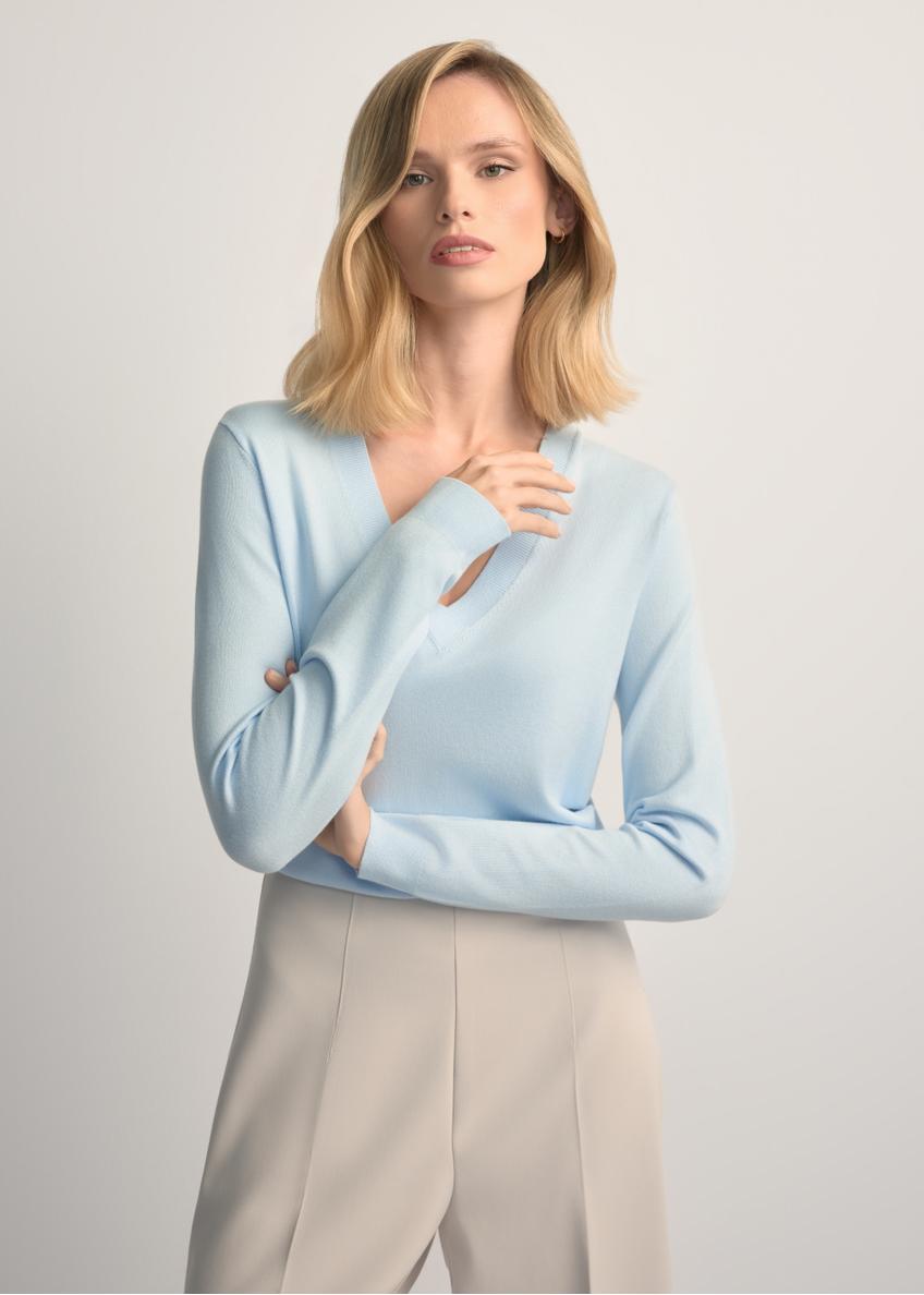 Svetlomodrý sveter s výstrihom do V SWEDT-0201-7A(W26) - pohľad spredu na výrobok, na modelke, na svetlom pozadí. Viditeľná polovica siluety.